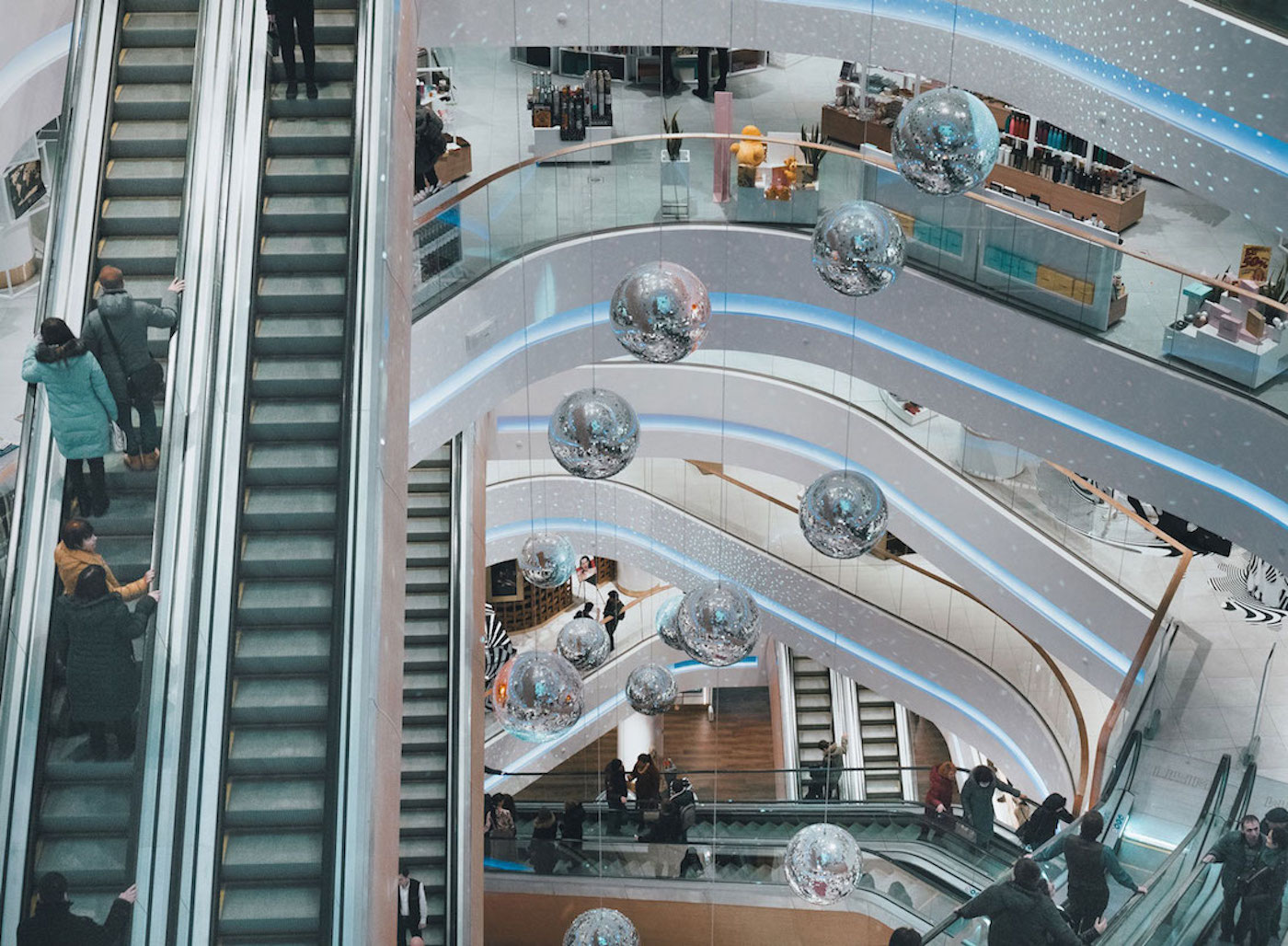 Einkaufszentrum mit glitzernden Discokugeln und Menschen auf einer Rolltreppe